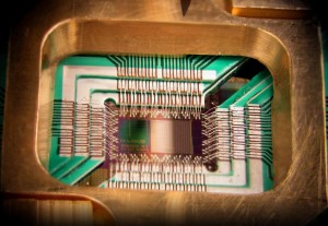 Photograph of a chip constructed by D-Wave Systems Inc., mounted and wire-bonded in a sample holder. The D-Wave processor is designed to use 128 superconducting logic elements that exhibit controllable and tunable coupling to perform operations.